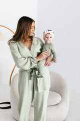 Adult in coordinating sage sleepwear holding a baby in the Bailey Onesie in Desert Sage and Clover, showing its long sleeves and contrasting foot cuffs.
